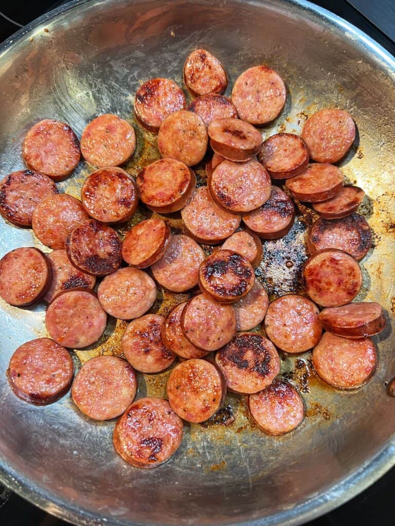 Andouille sausage cut into rounds and browning in a stainless steel pan.