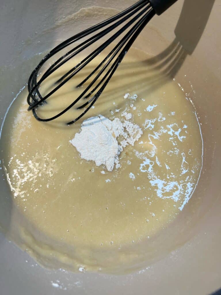 Use a black silicone whisk to whisk flour into a mixture of oil and butter in a pot. 