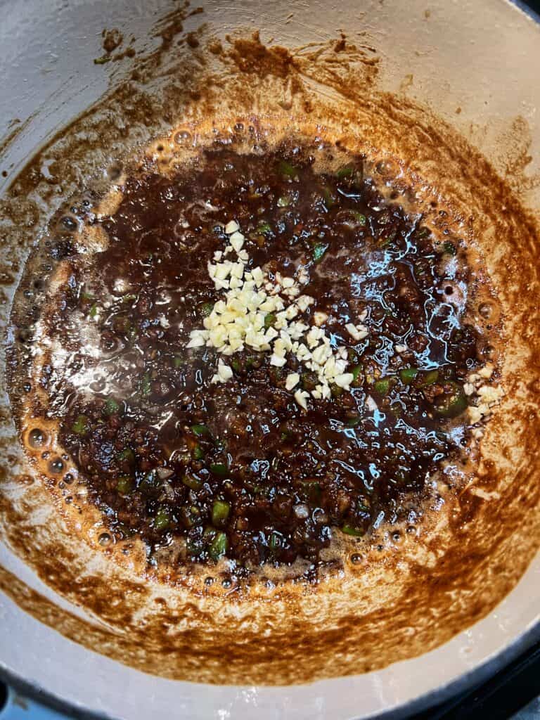 Minced garlic added into a dark roux. The roux is a very deep dark brown.
