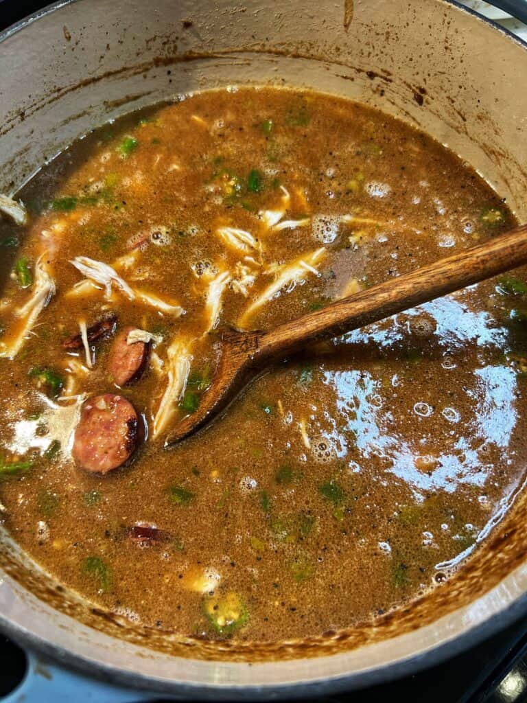 Andouille sausage and shredded chicken added to a gumbo base. The base is a deep brown color.