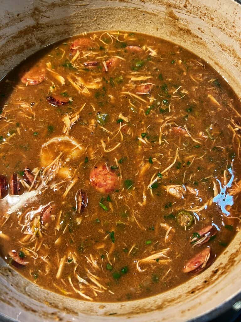 A pot of New Orleans Style Gumbo. The gumbo base is a dark brown color with shrimp, shredded chicken and andouille sausage.
