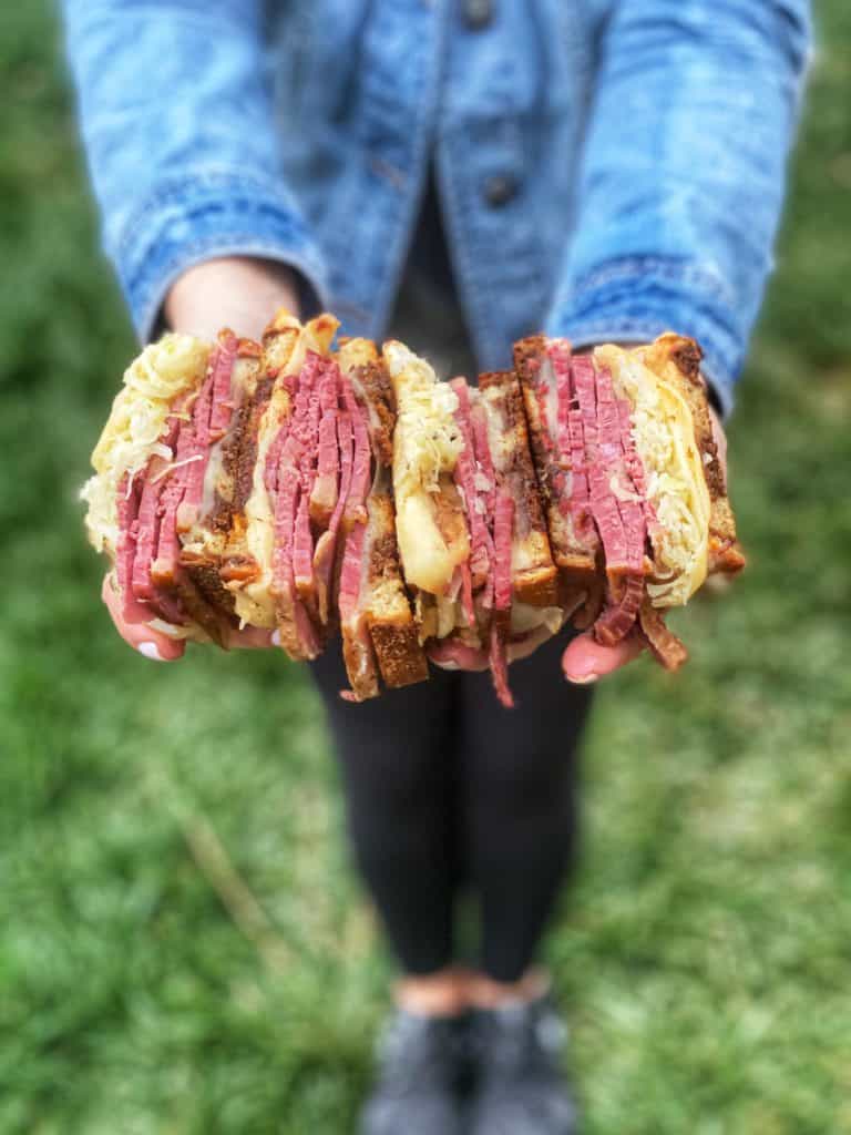 Me holding a two cheese reuben sandwich that has been cut four pieces. 