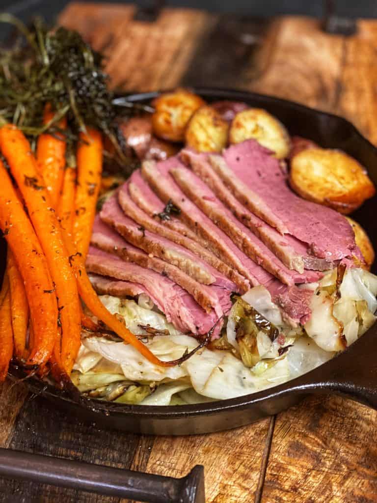 Sous vide corned beef sliced in a cast iron pan with carrots, cabbage and potatoes.