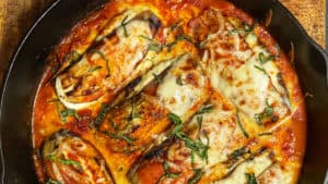 six eggplant Parmesan in a cast iron pan with sauce and cheese