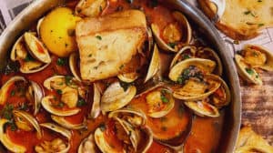 a pan of clams with chorizo in a tomato broth with toasted bread
