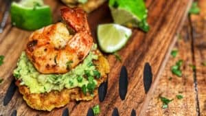 three tostones topped with guacamole and blackened shrimp on a wooden board