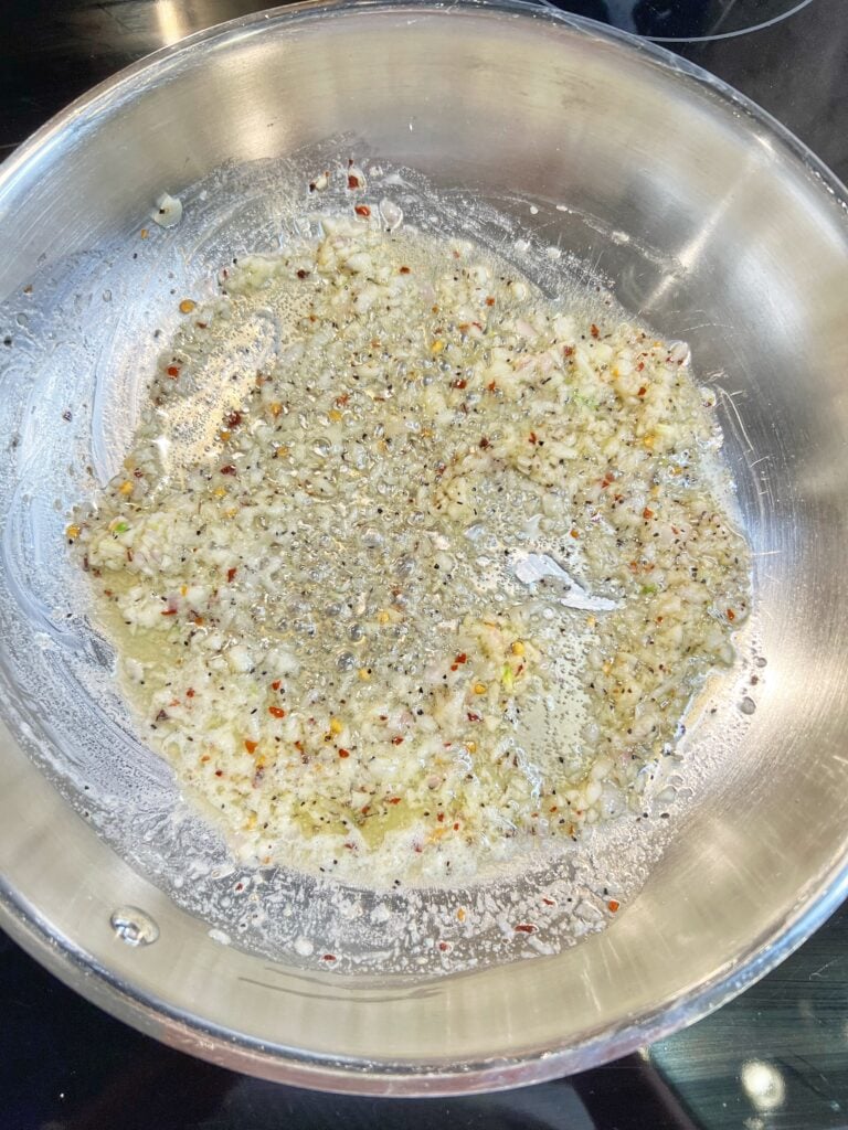Minced garlic and shallots sautéing in a stainless steel pan with butter.