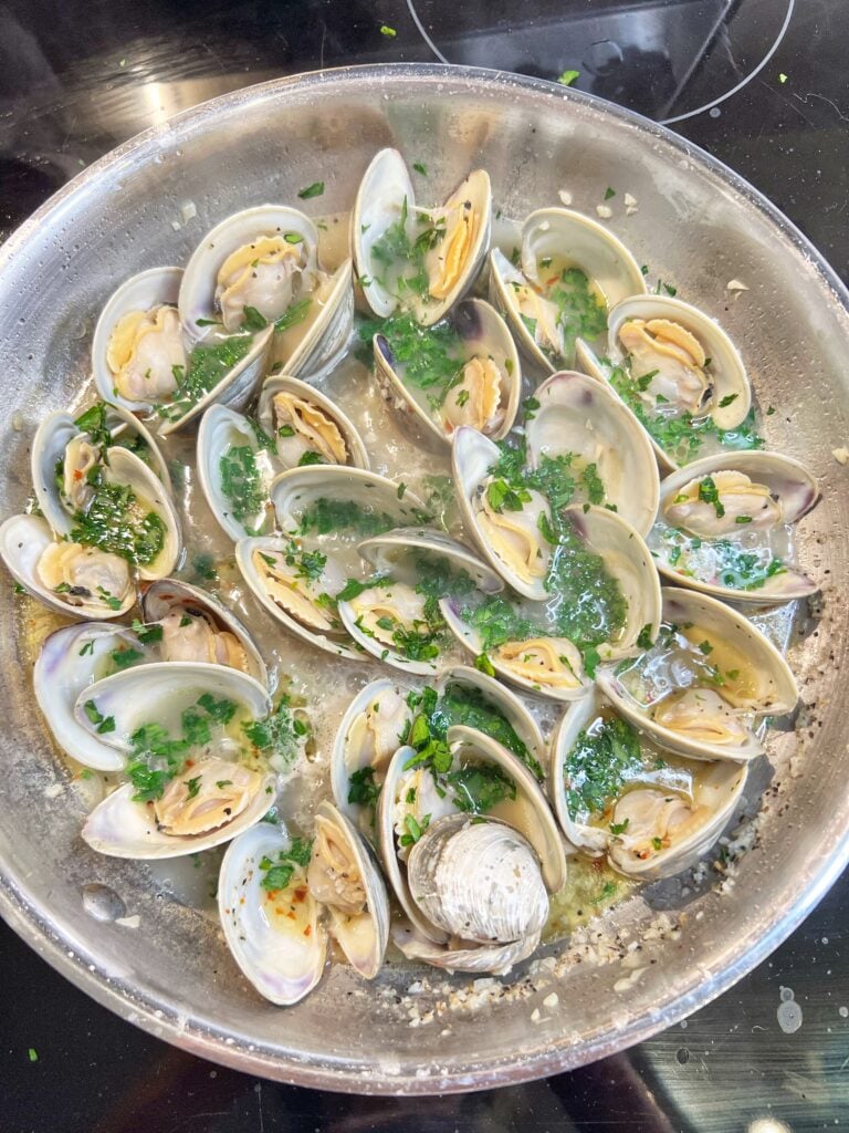 A pan of butter garlic steamed clams. The clams are open and swimming in a garlic butter sauce with fresh parsley.