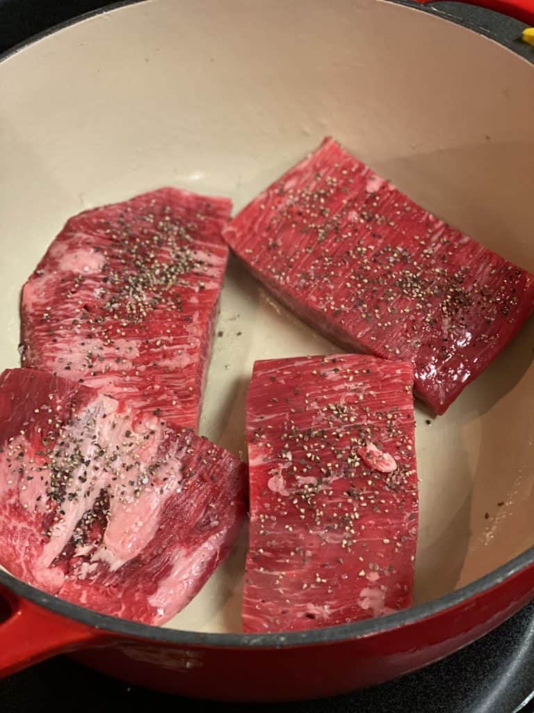 four pieces of flank steak in a cast iron pan for ropa vieja