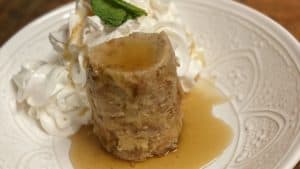 a piece of bread pudding in a white bowl with whipped cream and a mint leaf
