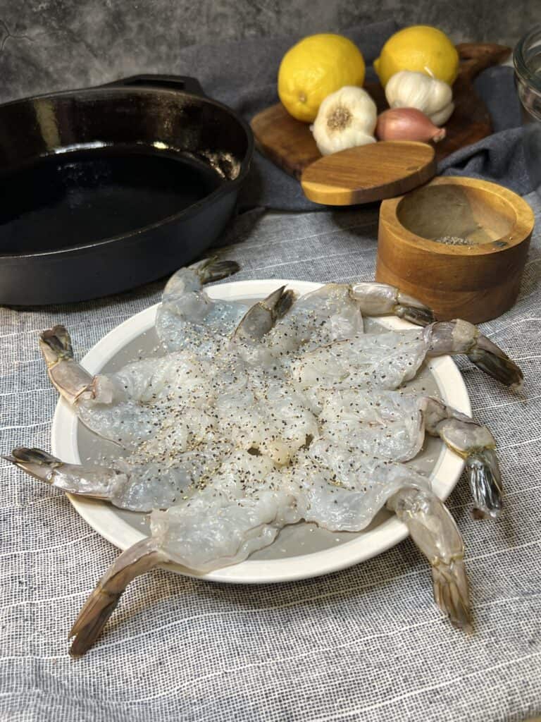 A grey plate with 9 butterflied shrimp with the tail on seasoned with salt and pepper.