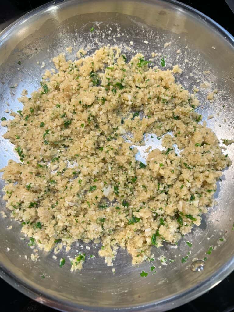 Toasted breadcrumbs and fresh parsley mixture in a stainless steel pan for stuffed shrimp