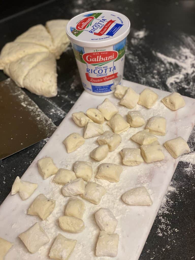raw homemade ricotta gnocchi pieces on a floured white marbled board