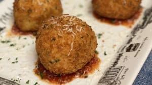 four balls of arancini sitting on a white platter with sauce