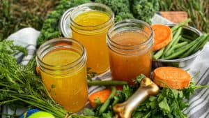 three ball jars of bone broth for dogs with carrots, tennis balls, and greens on a wooden platter