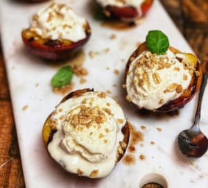 six grilled peaches on a marble board with ice cream on top