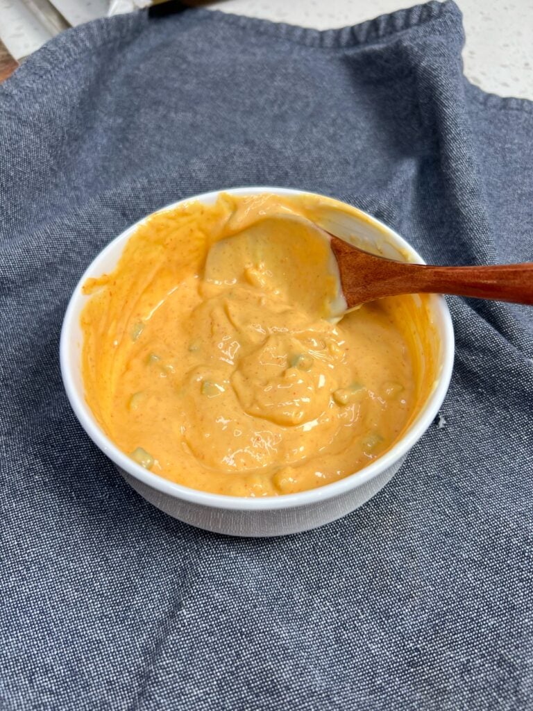 A mixture of mayo, Sriracha and diced jalapeño in a small white bowl. The sauce has an orangish hue.