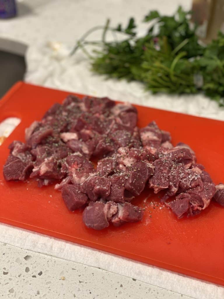 cubed lamb on a red cutting board