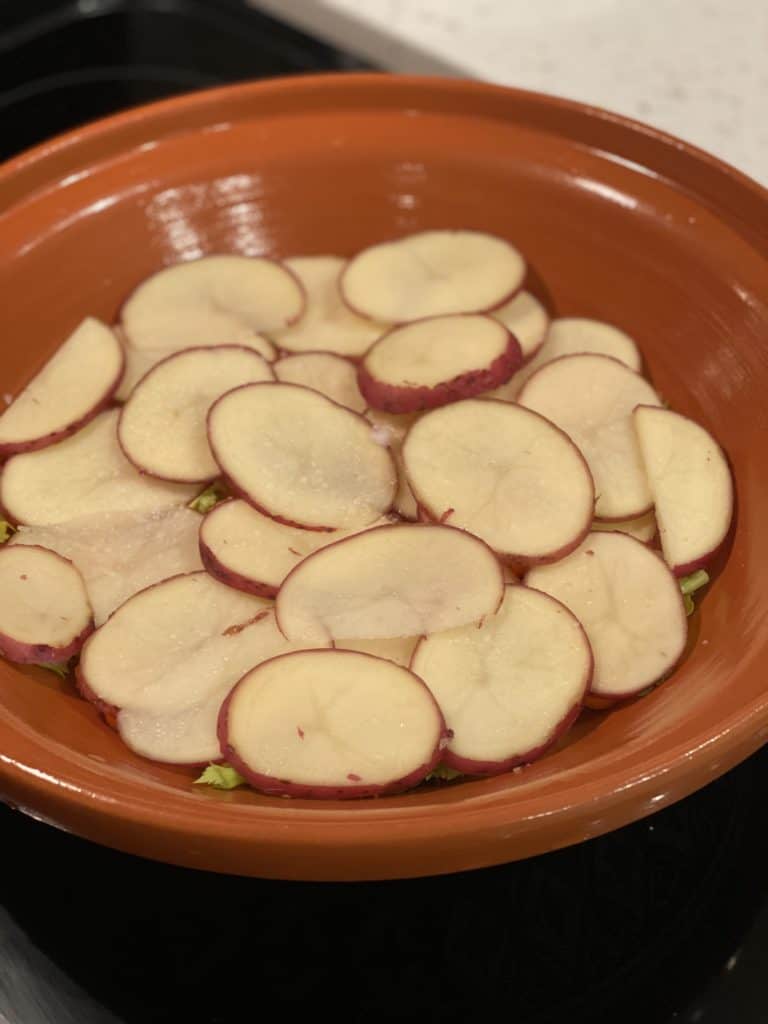 sliced potatoes on the bottom of an orange clay pot