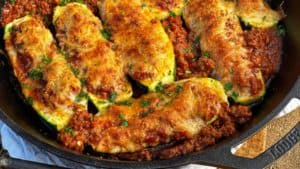 eight zucchini boats filled with meat and cheese in a cast iron pan