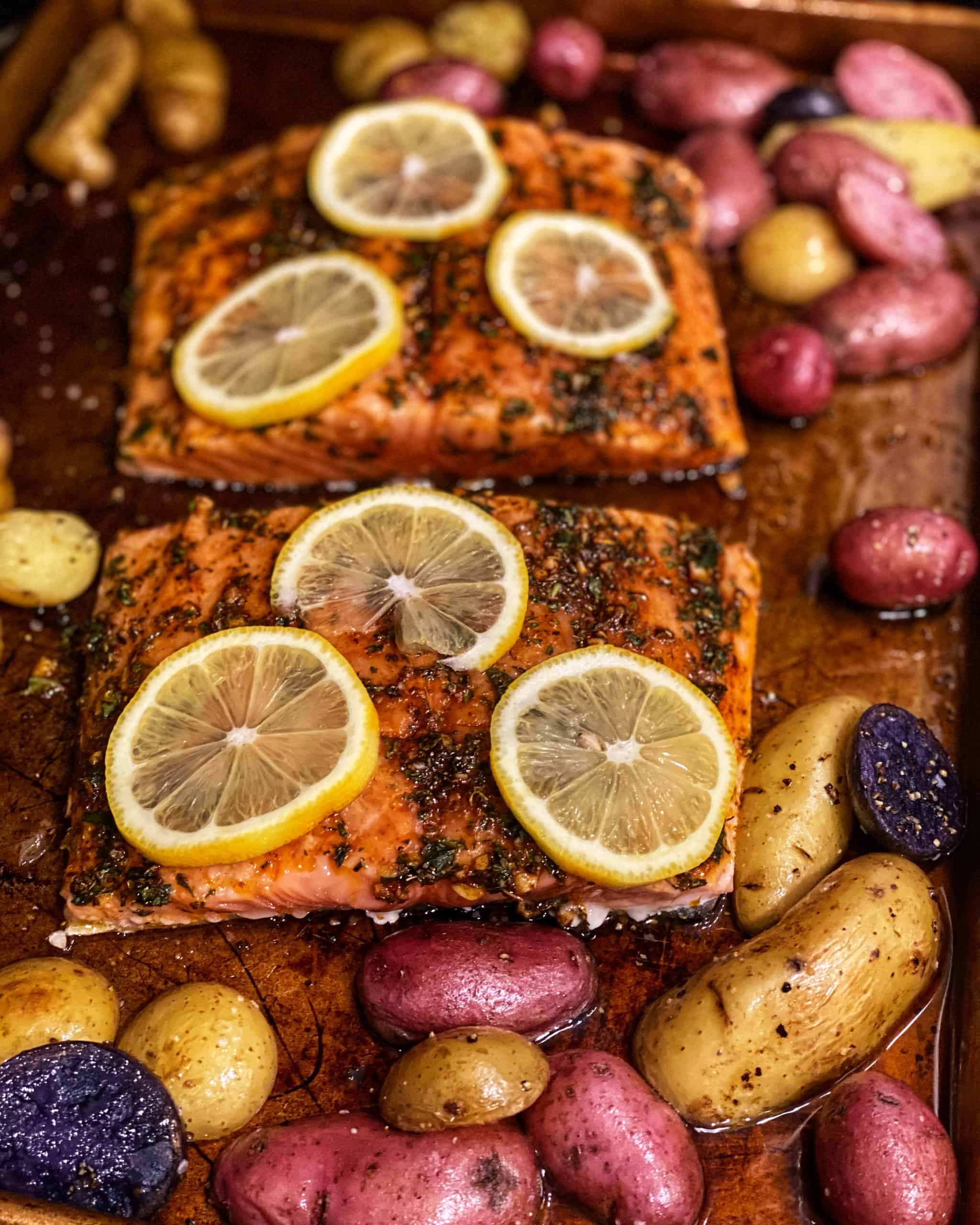 a pan of herb and honey glazed salmon topped with lemon slices surrounded by potatoes