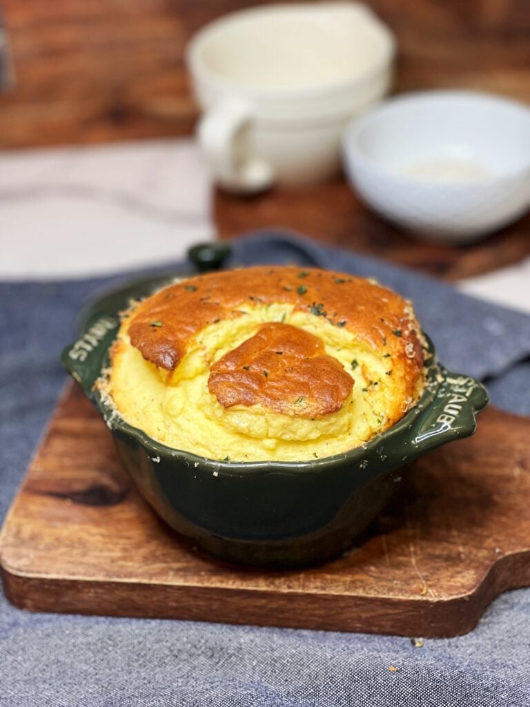 A small green French cocotte filled with a fluffy cheese soufflé. The soufflé has a browned top.