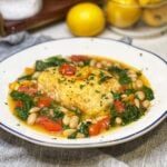 A piece of pan seared halibut in a spicy tomato broth with white beans and spinach.