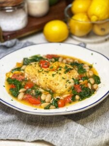 A piece of pan seared halibut in a spicy tomato broth with white beans and spinach.