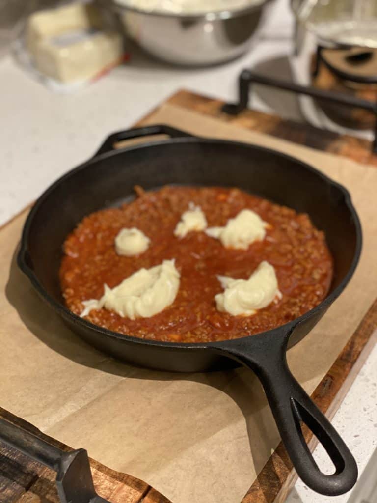 meat sauce dotted with béchamel sauce in a cast iron pan