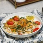 A white bowl of baked corvina with tomatoes. The fish is over a bed of rice with cherry tomatoes and garnished with fresh parsley.