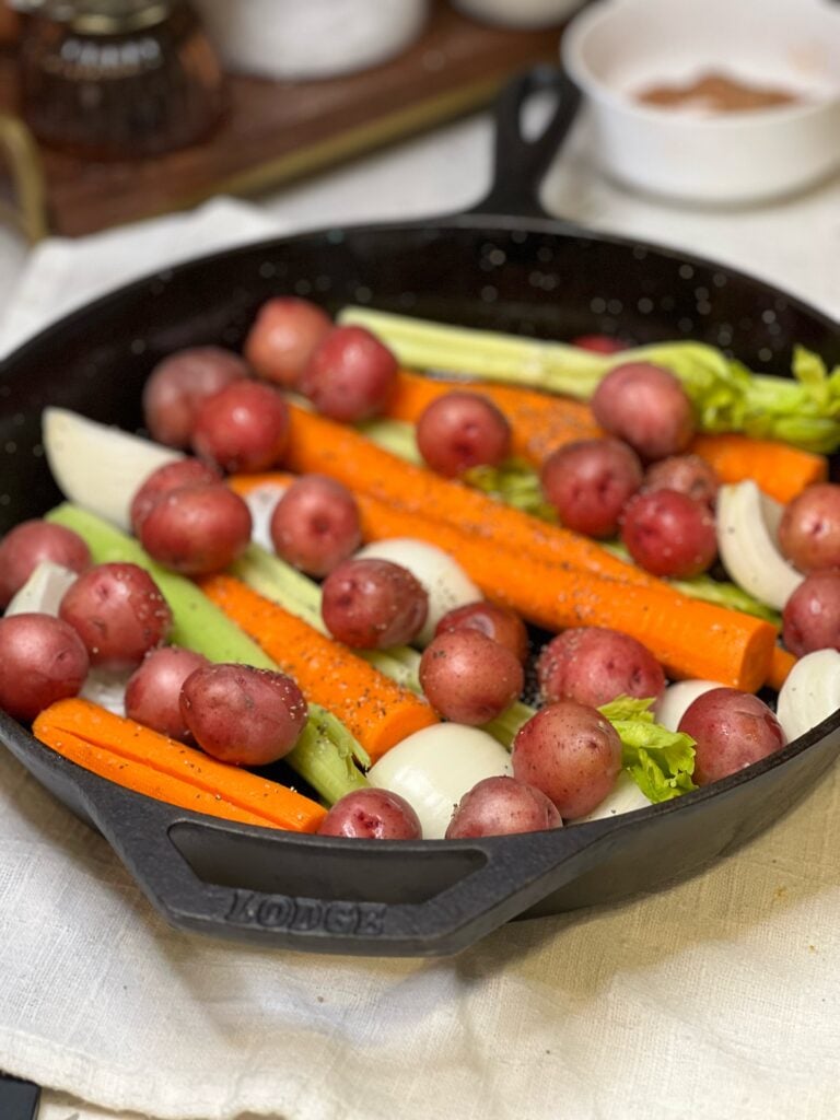 Carrots, quartered white onion, celery stalks and carrots in a cast iron pan.