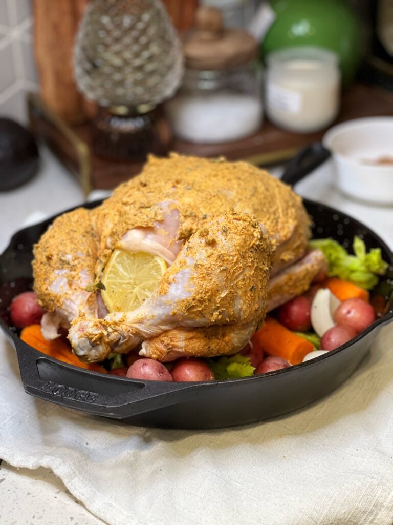 A whole chicken covered in her butter laying on a bed of vegetables ready to roast.
