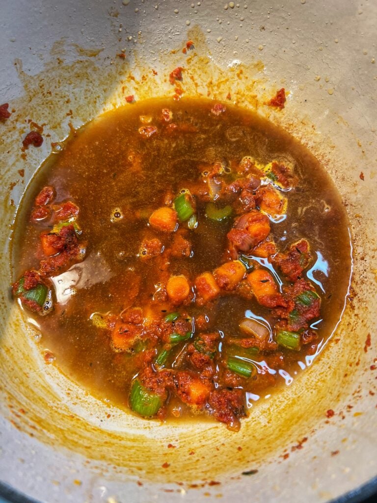 Lobster stock in a pot of sautéed vegetables and tomato paste.