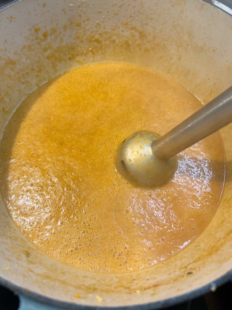 Blending the base of Lobster Bisque with an immersion in a stock pot. The color of the base is a golden, orange color.