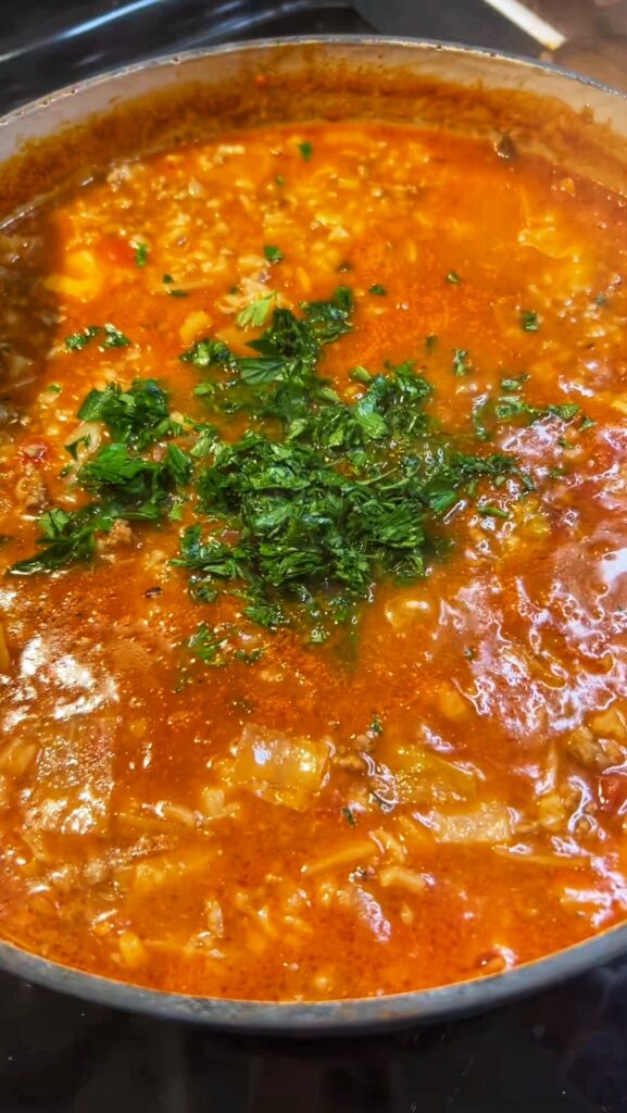 A pot of finished cabbage roll soup with fresh chopped parsley. The soup is red in color.