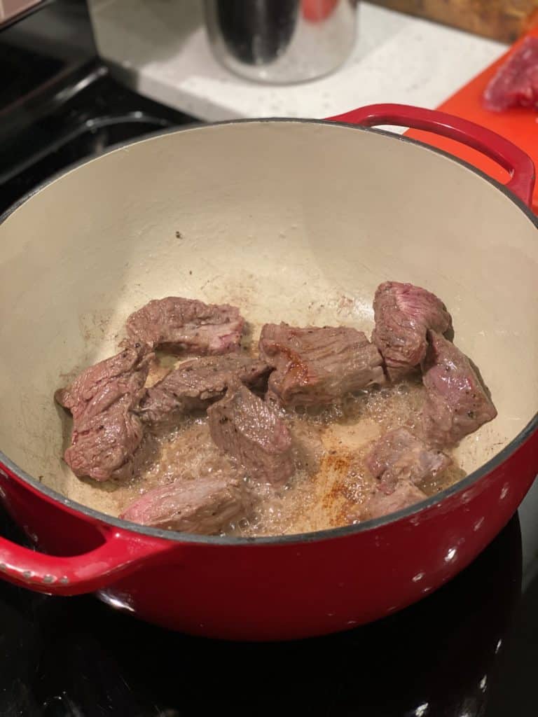 beef chunks searing in a red enameled cast iron pot