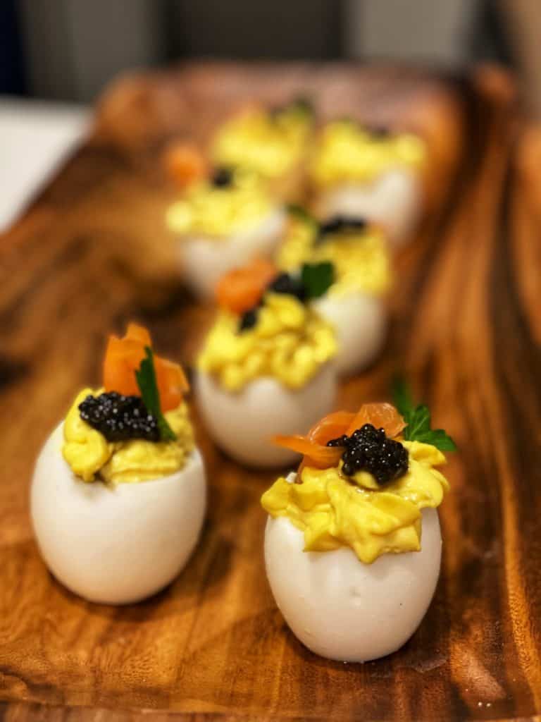six fancy deviled eggs sitting in a long wooden platter