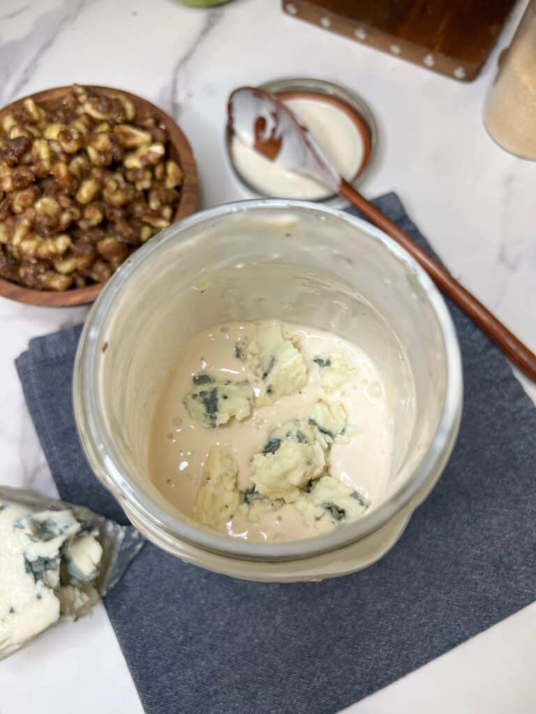 Crumbled Roquefort cheese sitting in a creamy white salad dressing base in a large glass jar.