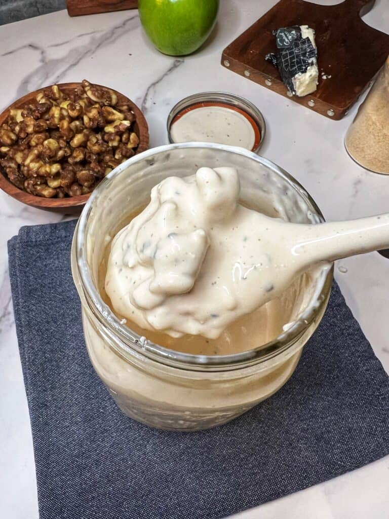 Spooning out a creamy dressing with Roquefort cheese chunks out of a glass jar.