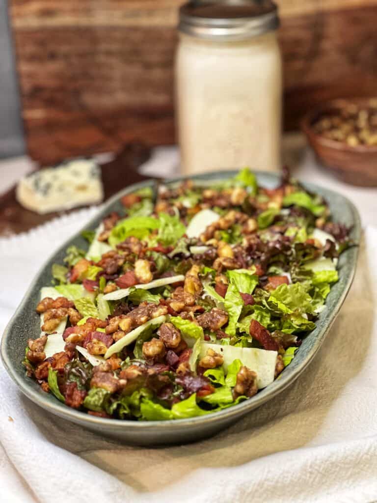 Romaine lettuce, red lettuce, crisp bacon pieces and candied walnuts together in a green platter.