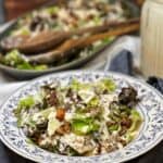 A blue flowered plated holding a serving of a Red Roquefort Salad. The salad includes chopped Romaine, chopped red lettuce, covered in a creamy white dressing and topped with crisp bacon and candied walnuts.
