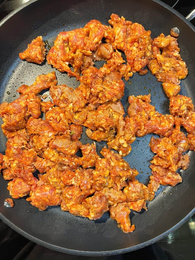 Hot sausage broken up and cooking in a non-stick pan.