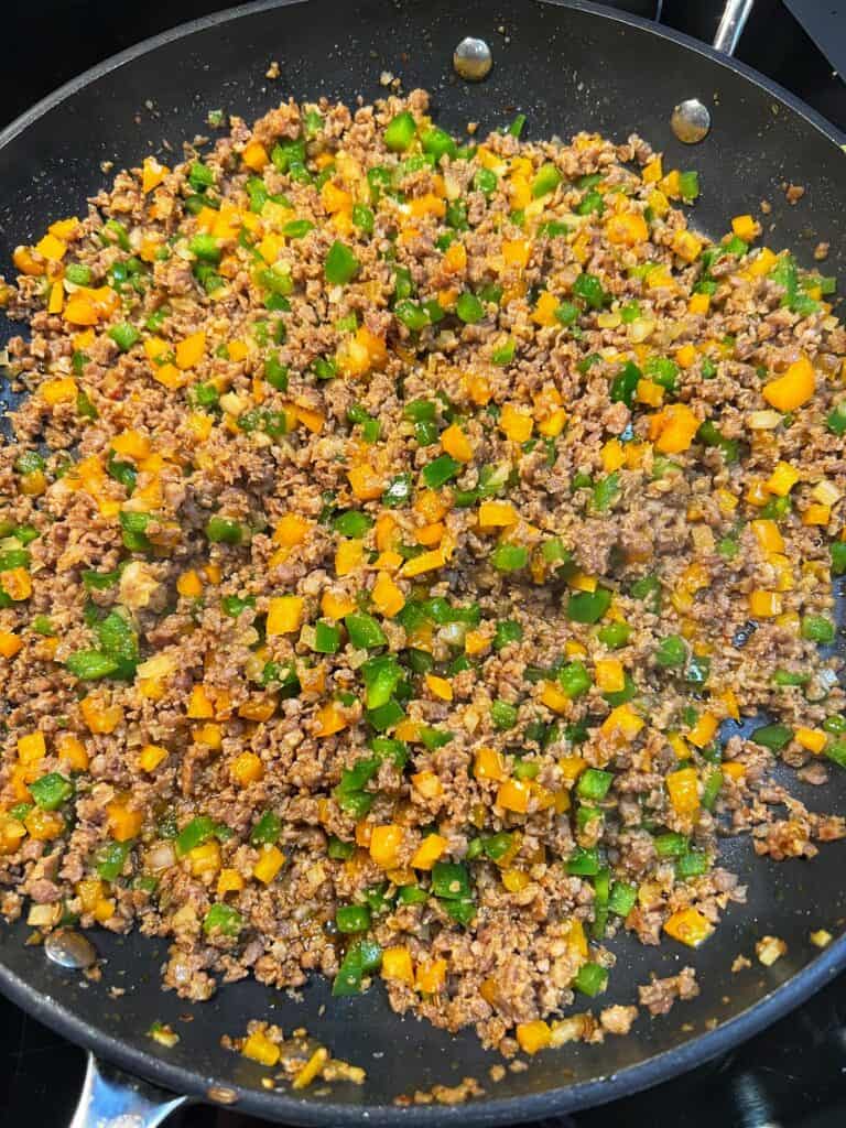 Cooked sausage and pepper filling for egg rolls in a non-stick pan.