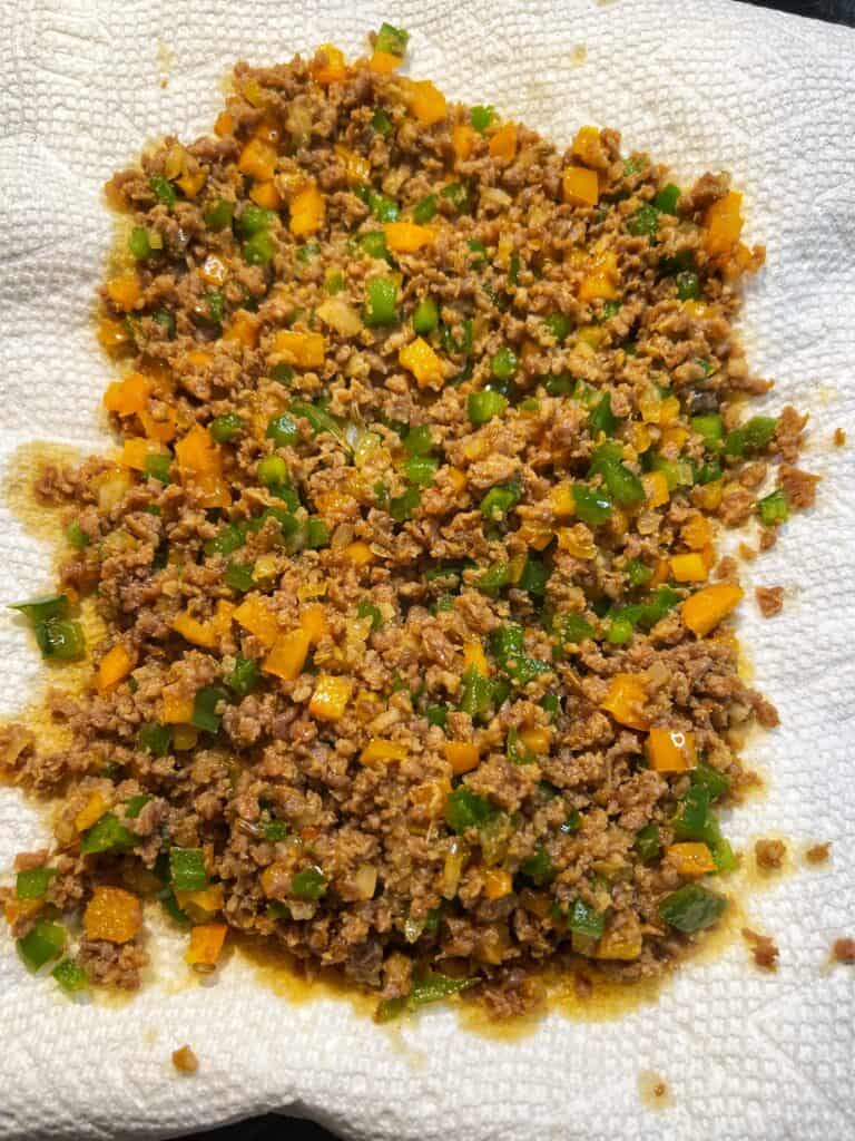 Filling for sausage and peppers egg rolls draining on paper towels.