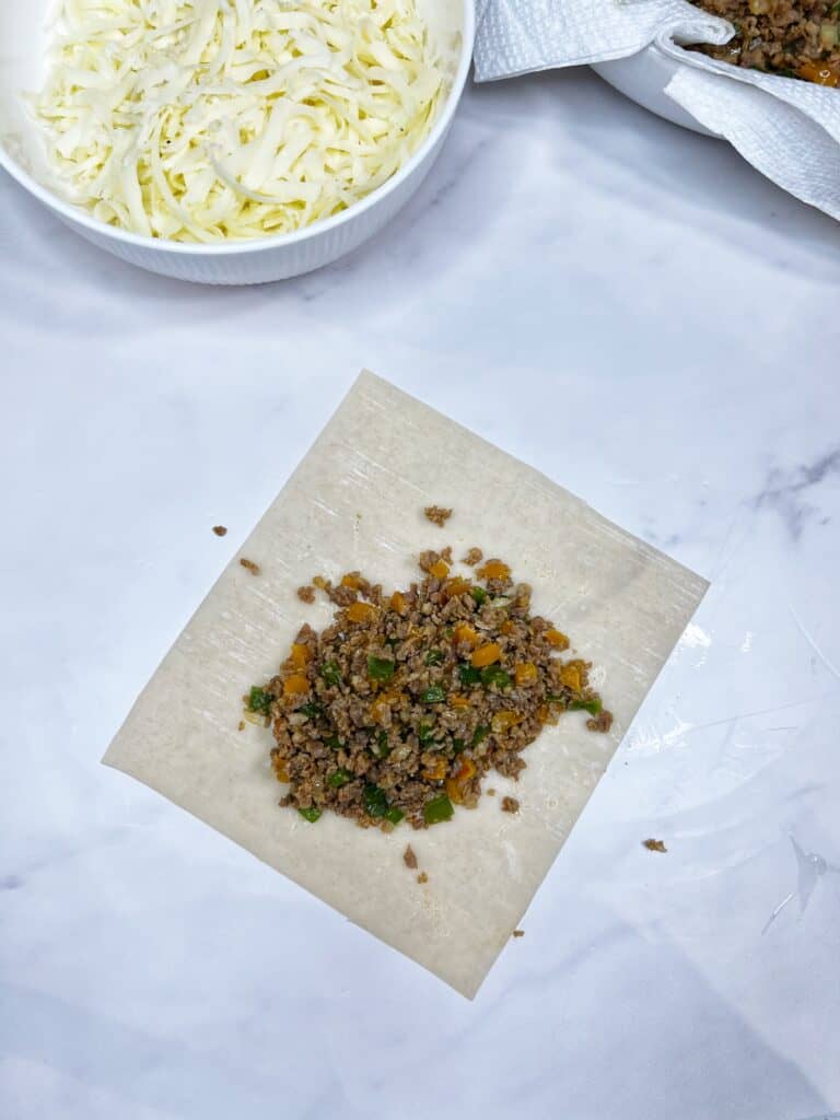 Sausage and pepper filing adding to a corner of an egg roll wrapper.
