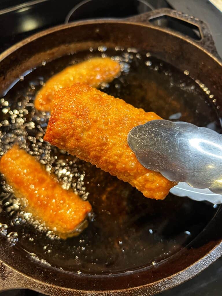Holding a deep fried egg roll with a pair of tongs.