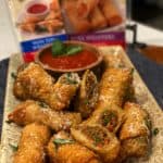 A platter of sausage and peppers egg rolls with a bowl of marinara sauce.