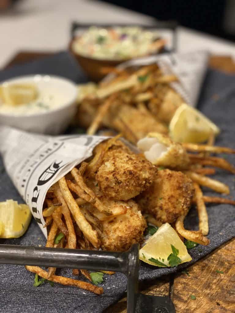 fish and chips in newspaper cones laying on a wooden board garnished with lemon wedges