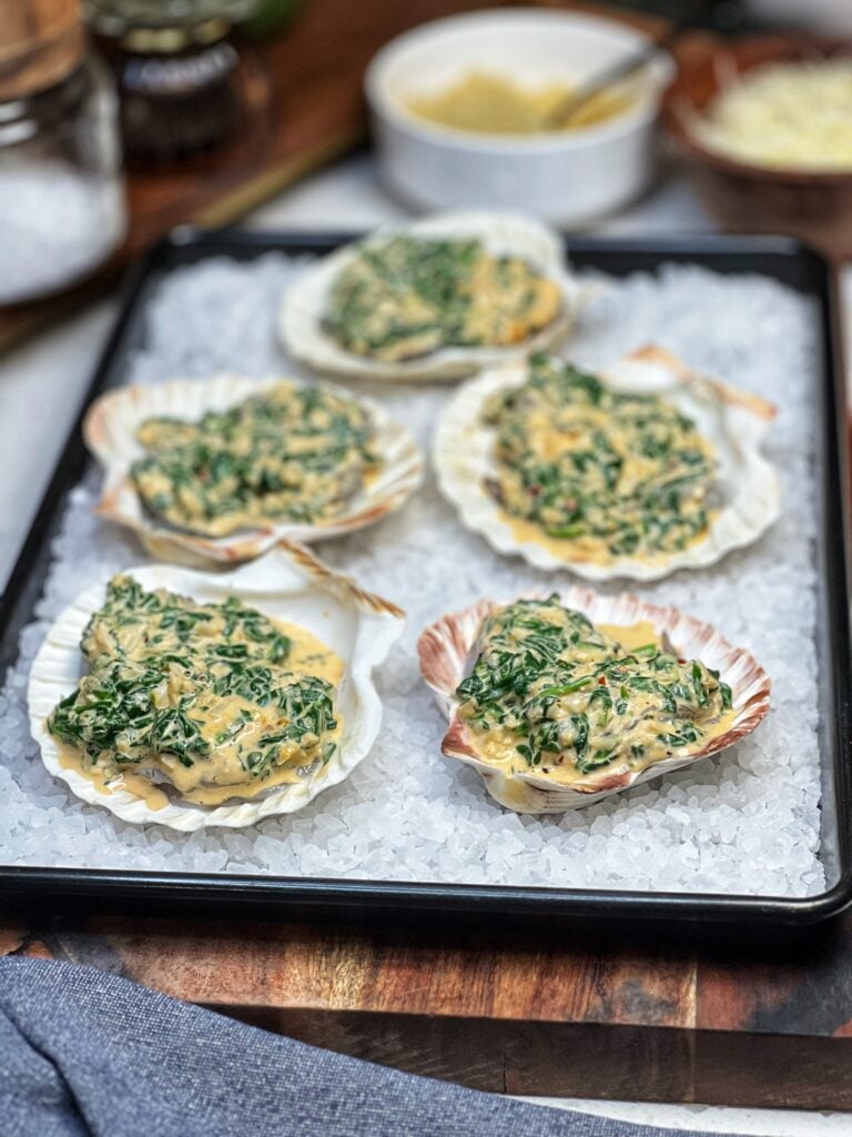 Five shrimp filled scallop shells. Each shell is topped with a tomato cream spinach sauce. This is the base layer for Shrimp Rockefeller.