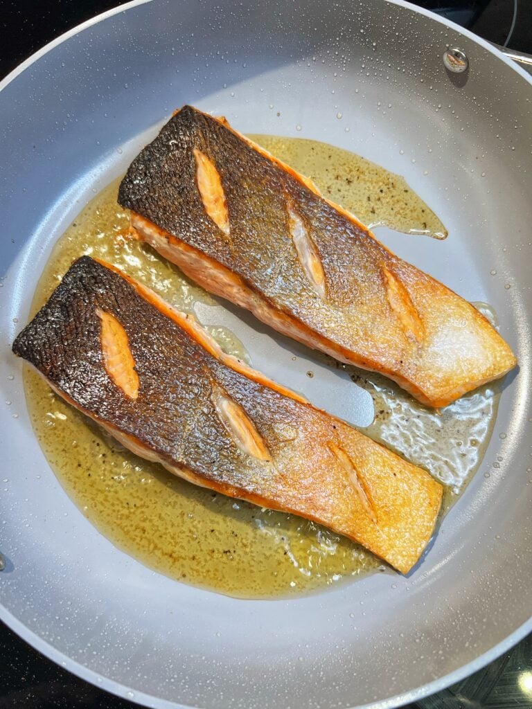 Two filets of salmon in a non-stick pan showing the crispy skin.